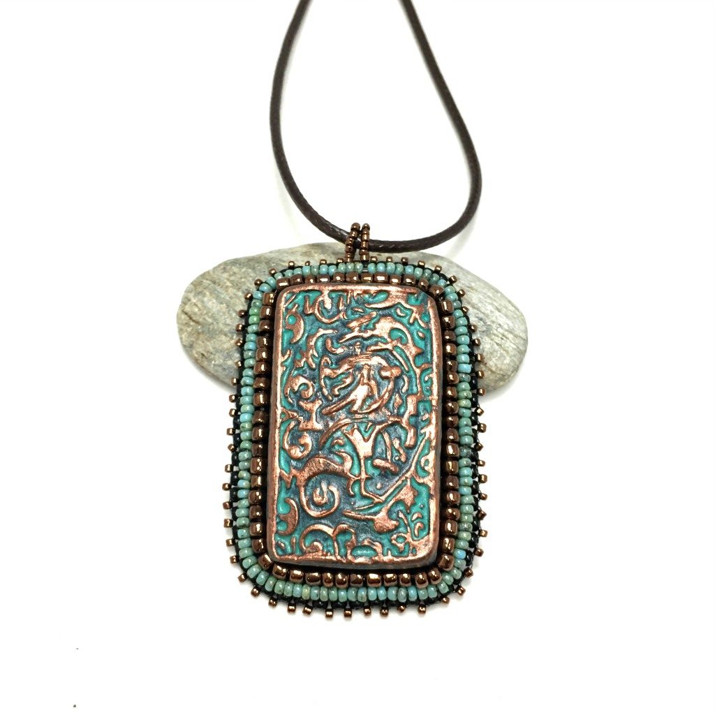 Large copper patina textured floral Rectangle pendant with turquoise and bronze beaded edging on a brown cord necklace chain.