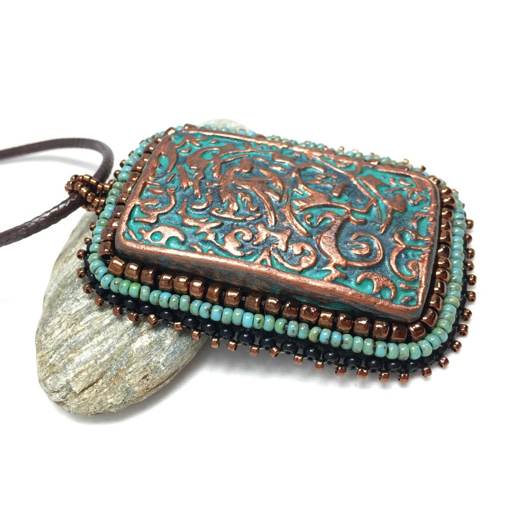 Right view of large copper patina textured floral Rectangle pendant with turquoise and bronze beaded edging on a brown cord necklace chain.