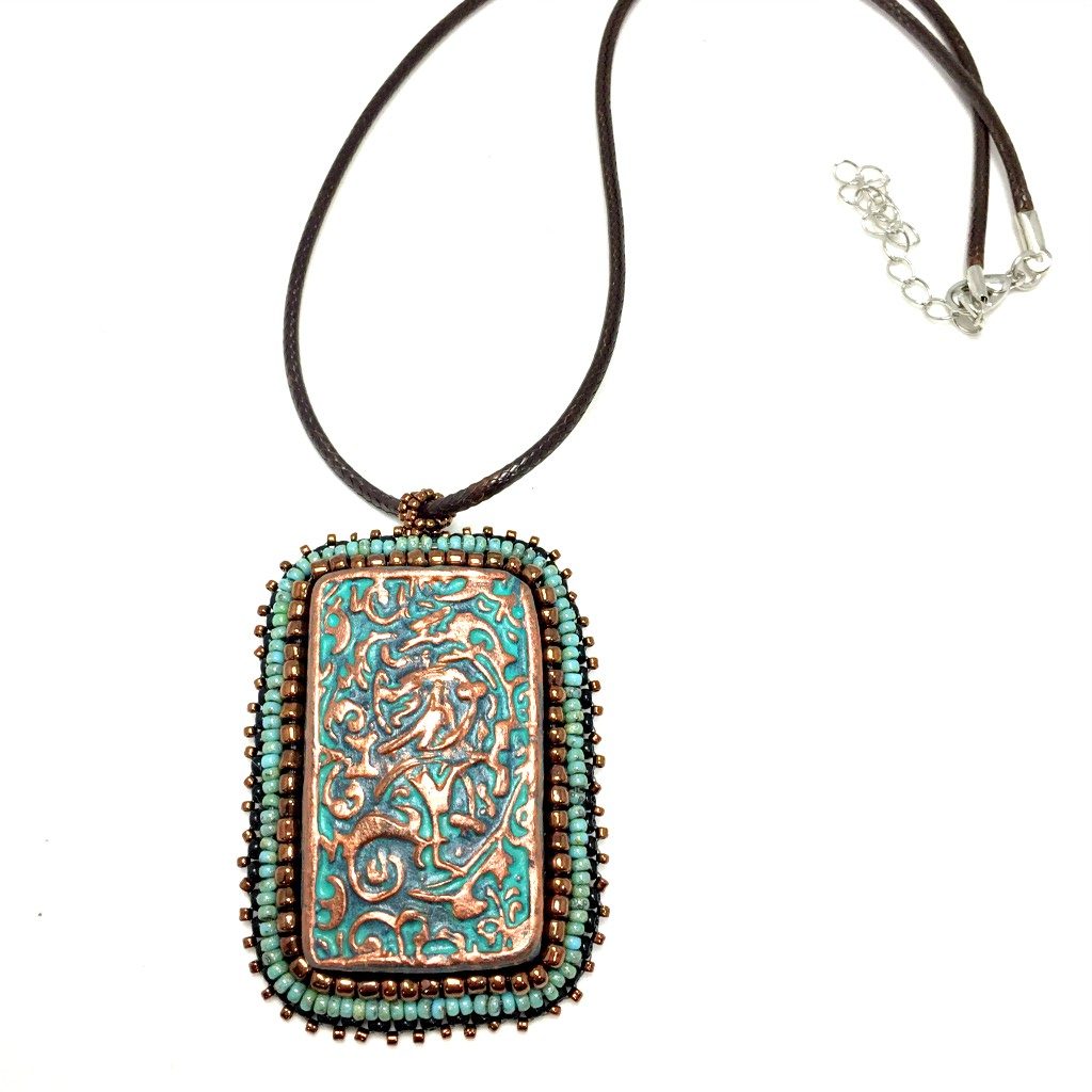Large copper patina textured floral Rectangle pendant with turquoise and bronze beaded edging on a brown cord necklace chain.