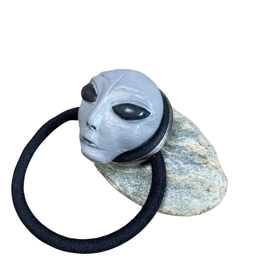 Side profile view of an gray alien, head hair tie, resting on a rock