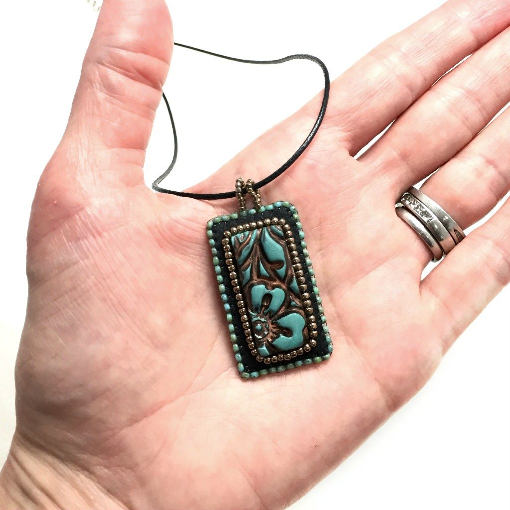 A rectangle Patina Flower beaded Necklace held in a hand for size reference.