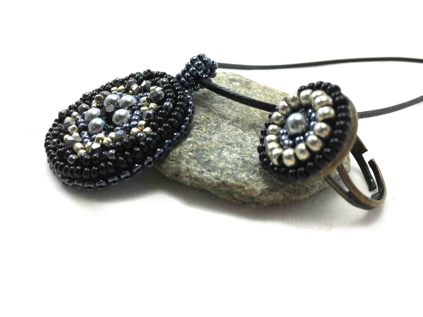 Side profile of Mandala beaded pendant necklace and ring set in black and silver leaning on a pebble.