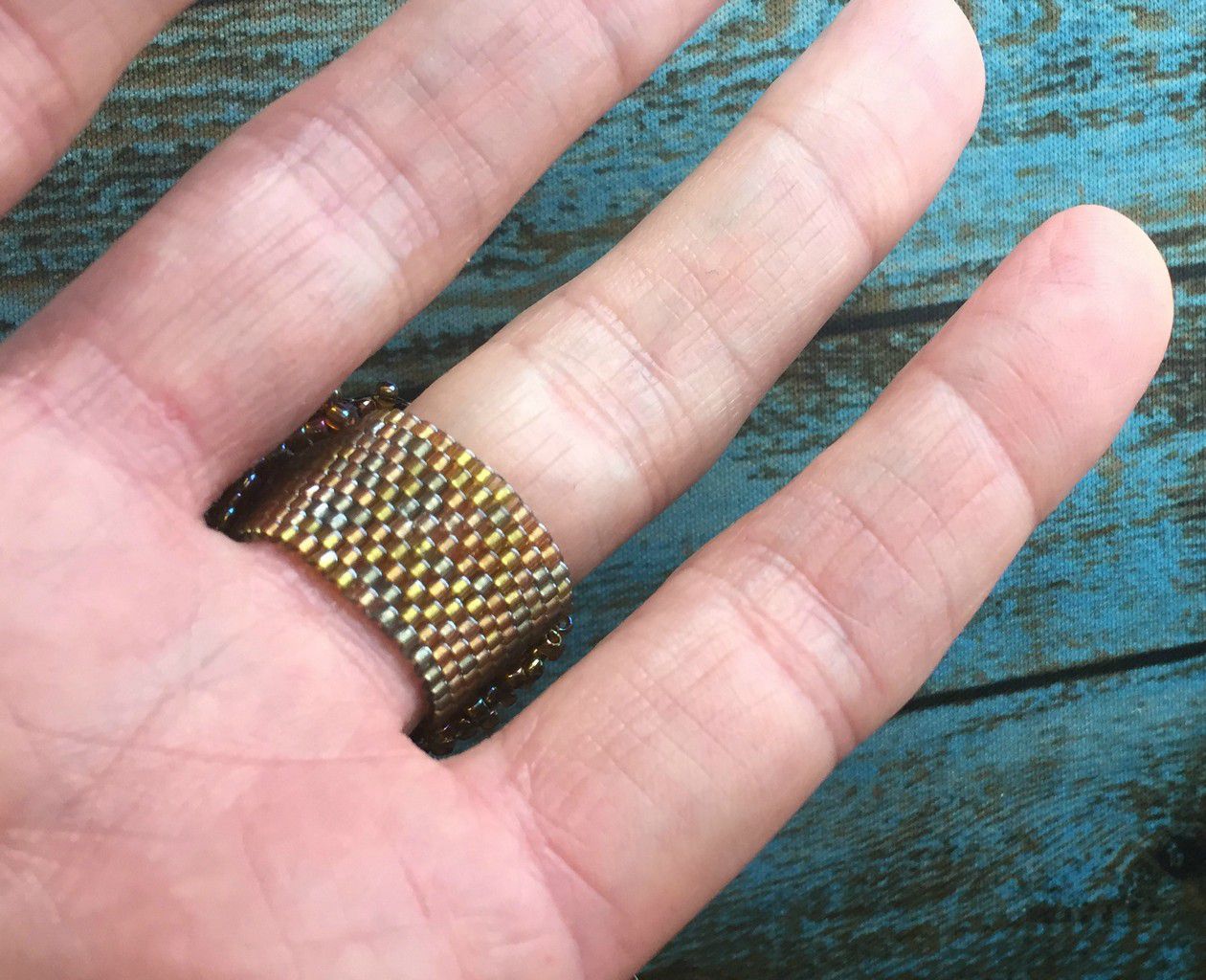 View of beaded band on a hand of the sun face wide fashion ring with gold, purple and bronze microbeaded band and bezel