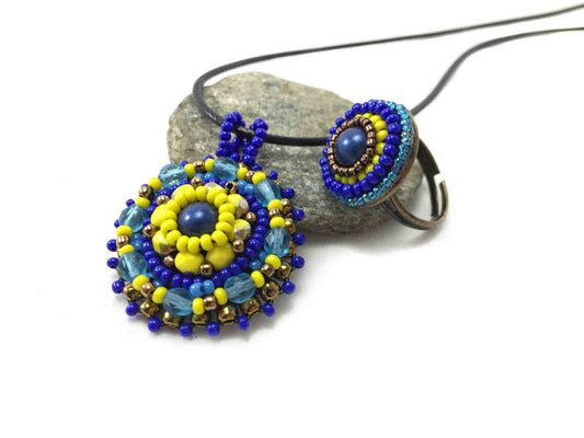 Beaded Mandala pendant necklace and ring set in blue and yellow resting in a pebble.