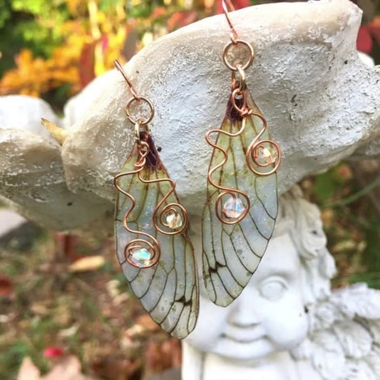 yellow cicada wing earrings with copper wire swirls with crystals hanging from a garden ornament outside in a garden.