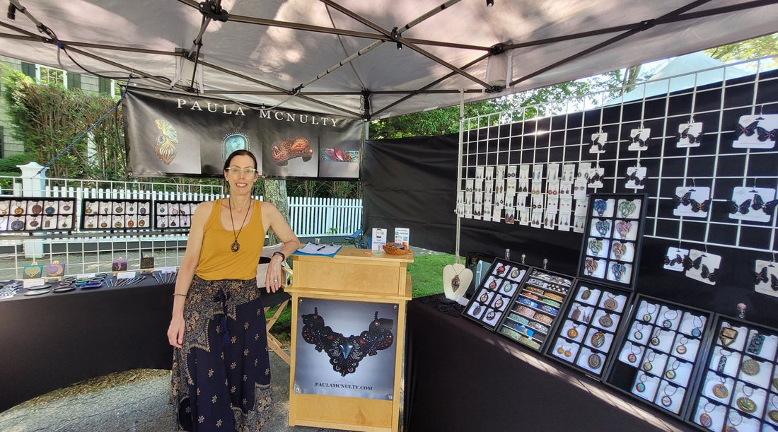 Woman standing next to a checkout booth within an outdoor booth with jewelry displays at a art market