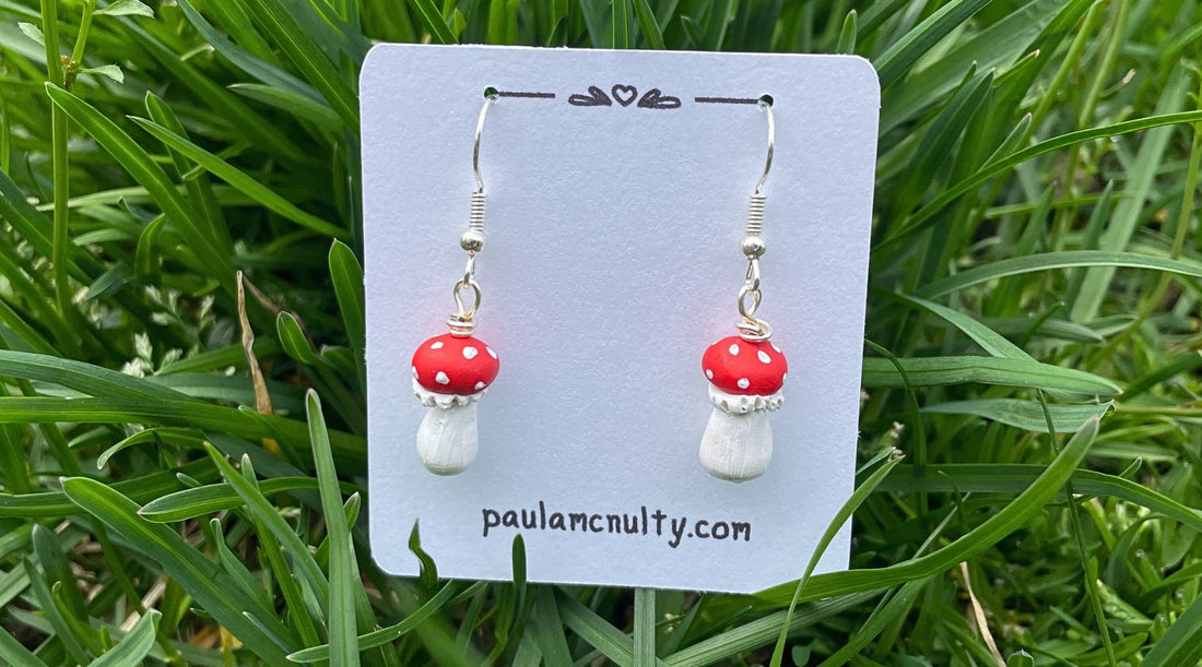 Mini red capped mushroom earrings on an earring card nestled in grass.
