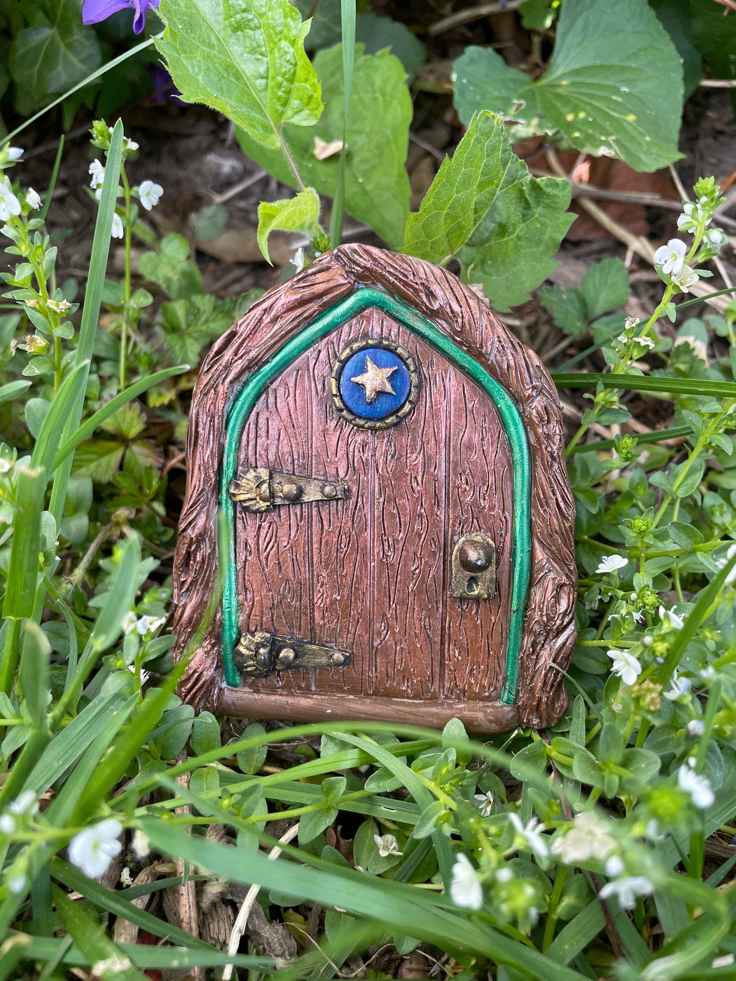 Small decorative fairy door in grassy area with flowers
