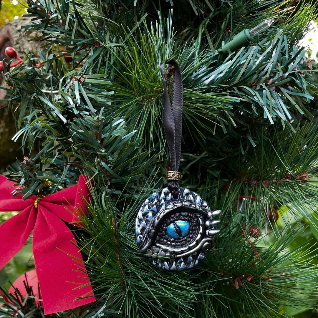A round dragon eye ornament with metallic silver and blue coloring with black satin ribbon hanging on a Christmas tree.