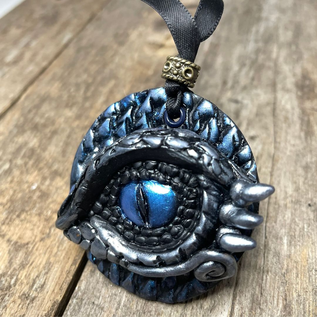 A round dragon eye ornament with metallic silver and blue coloring with black satin ribbon held in a hand
