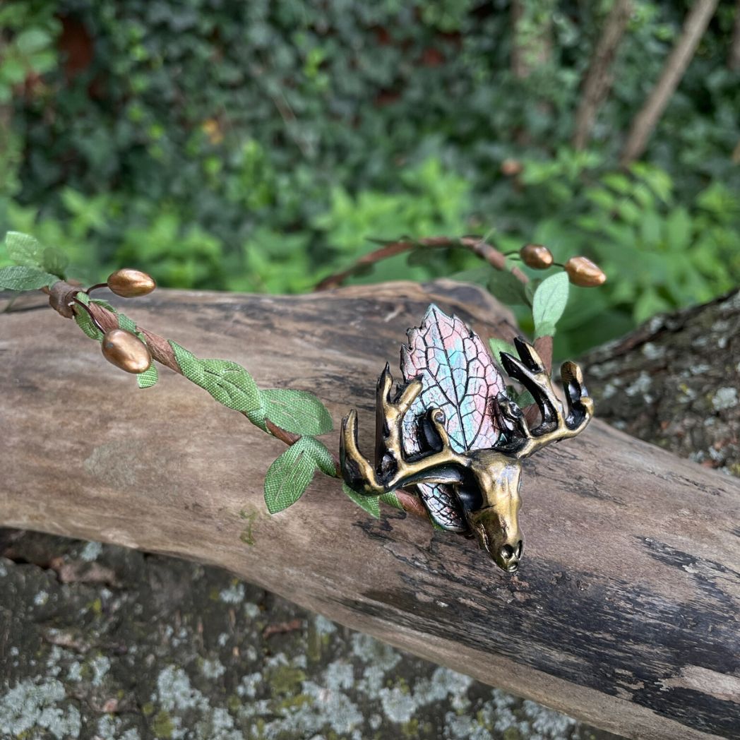 A wire crown with green leaves and a polymer clay leaf and elk focal on a tree branch.