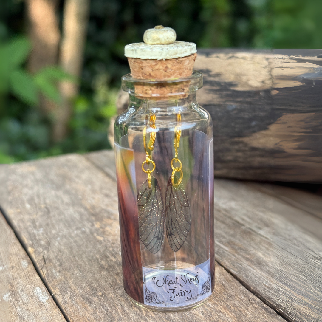 wheat sheaf fairy wing earrings inside a decorative bottle in a garden setting