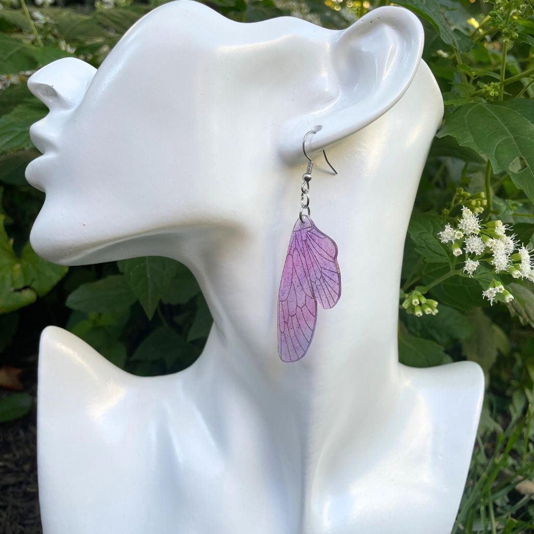 pink and purple sparkly glitter plastic fairy wing earrings hanging from an earring jewelry bust for size comparison