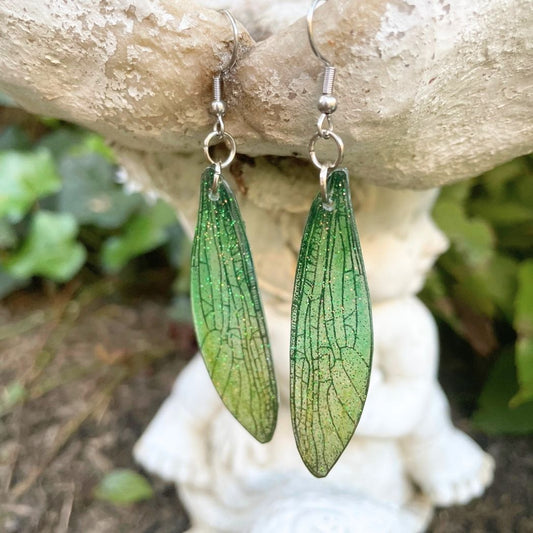 Sparkly glitter green dragonfly wing earrings hanging from a garden ornament.