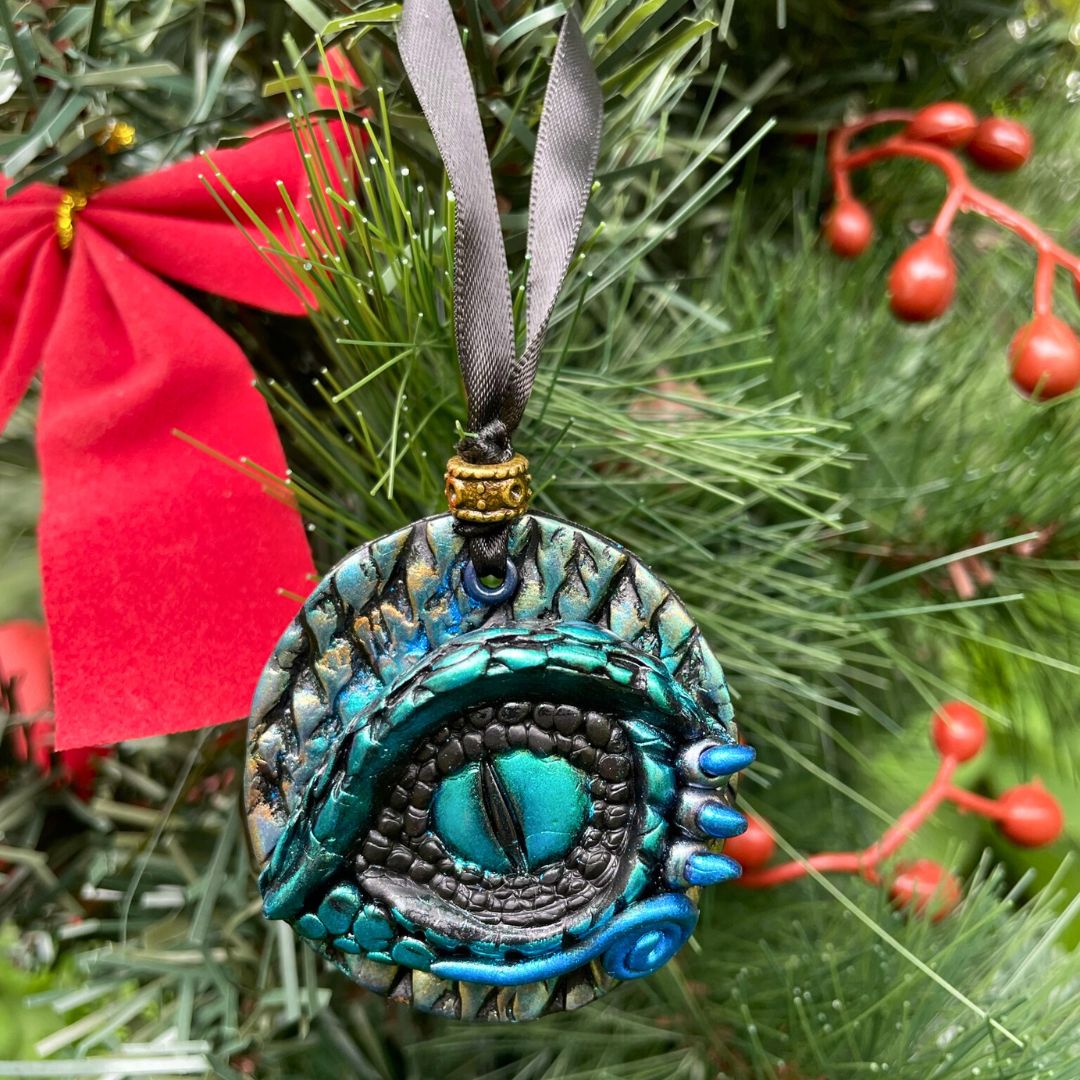 A round dragon eye ornament with metallic green gold and blue coloring with black satin ribbon hanging on a Christmas Tree