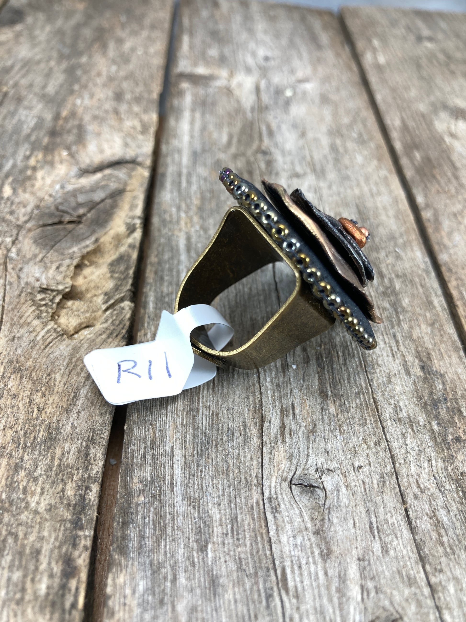 Side profile of Round statement ring with abstract hammered copper and silver clay with dark gold beaded edge