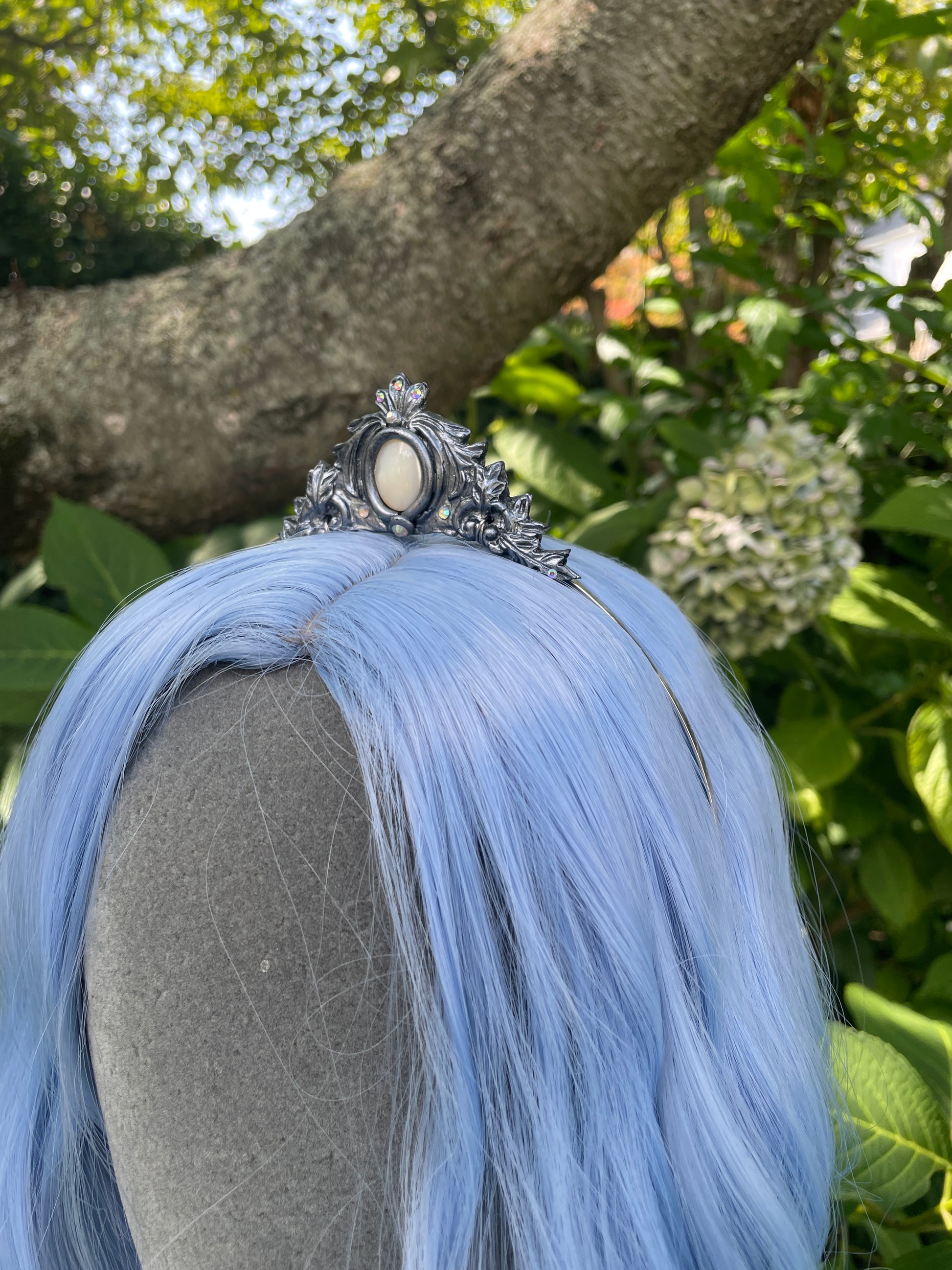 Side profile of a Silver mother of pearl mermaid crown on a model with blue hair in a garden