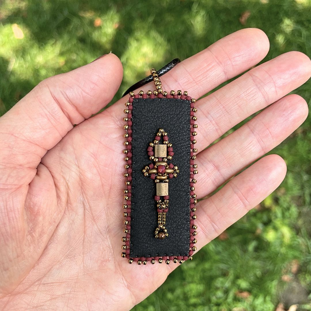 Red and gold Medieval Beaded faux leather rectangle pendant with beaded edge. held in a hand