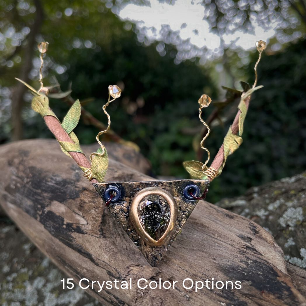 Teadrop crystal focal crwon with brown branches and green fabric leaves. Wired crystals around the sides. Crown sitting on a tree branch.