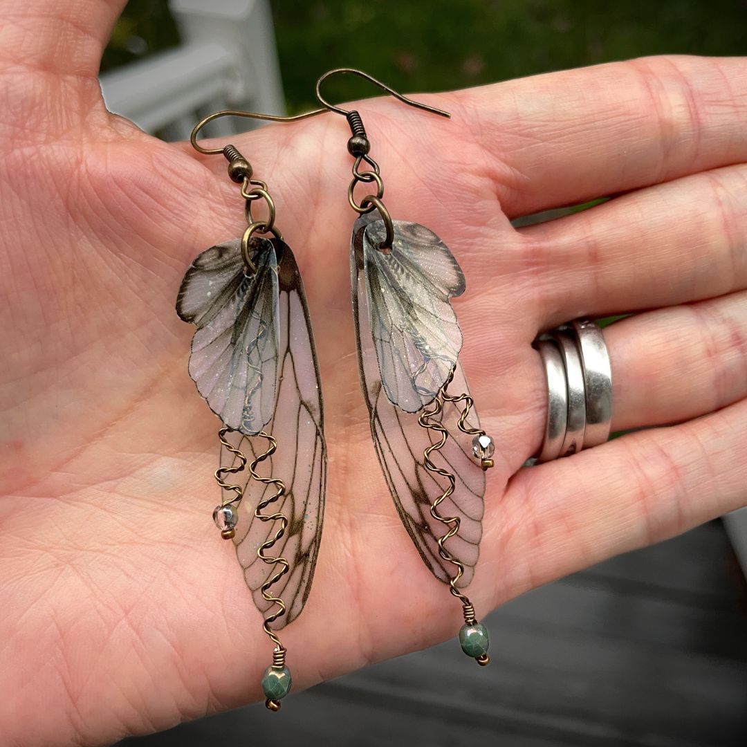 olive green butterfly earrings held in a hand.