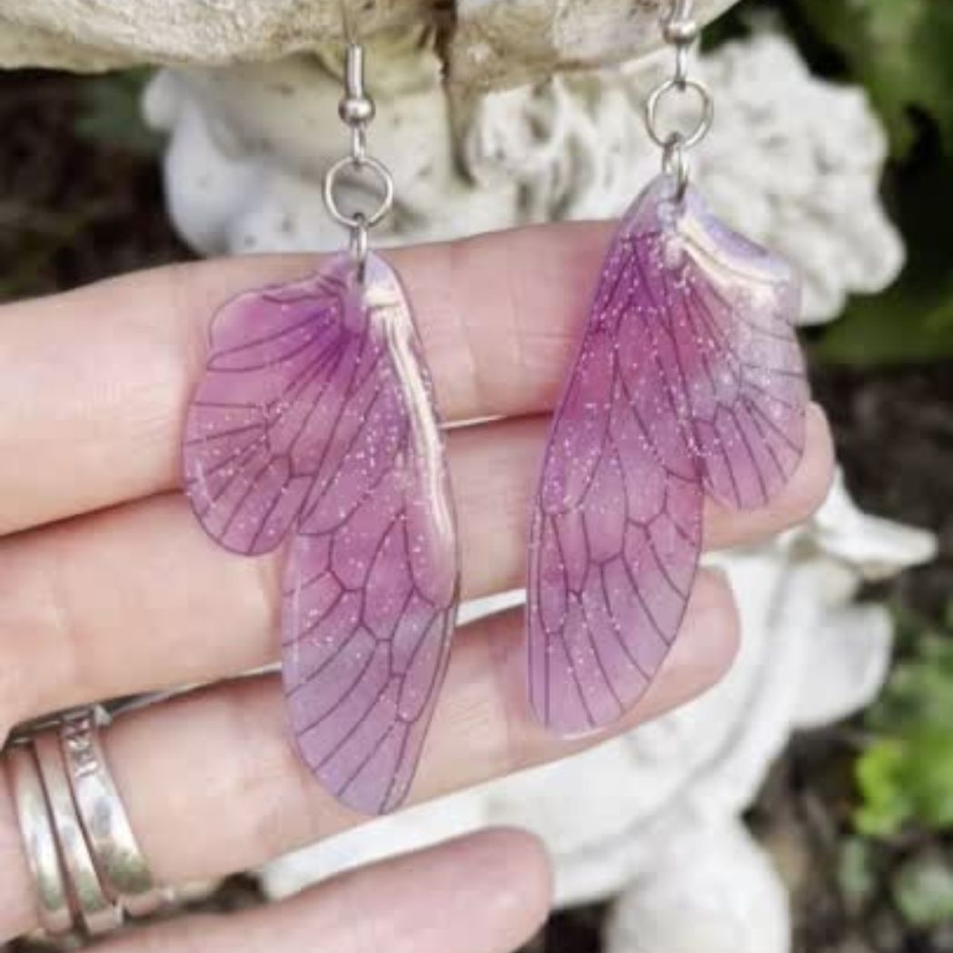 pink and purple sparkly glitter plastic fairy wing earrings held in a hand for size comparison