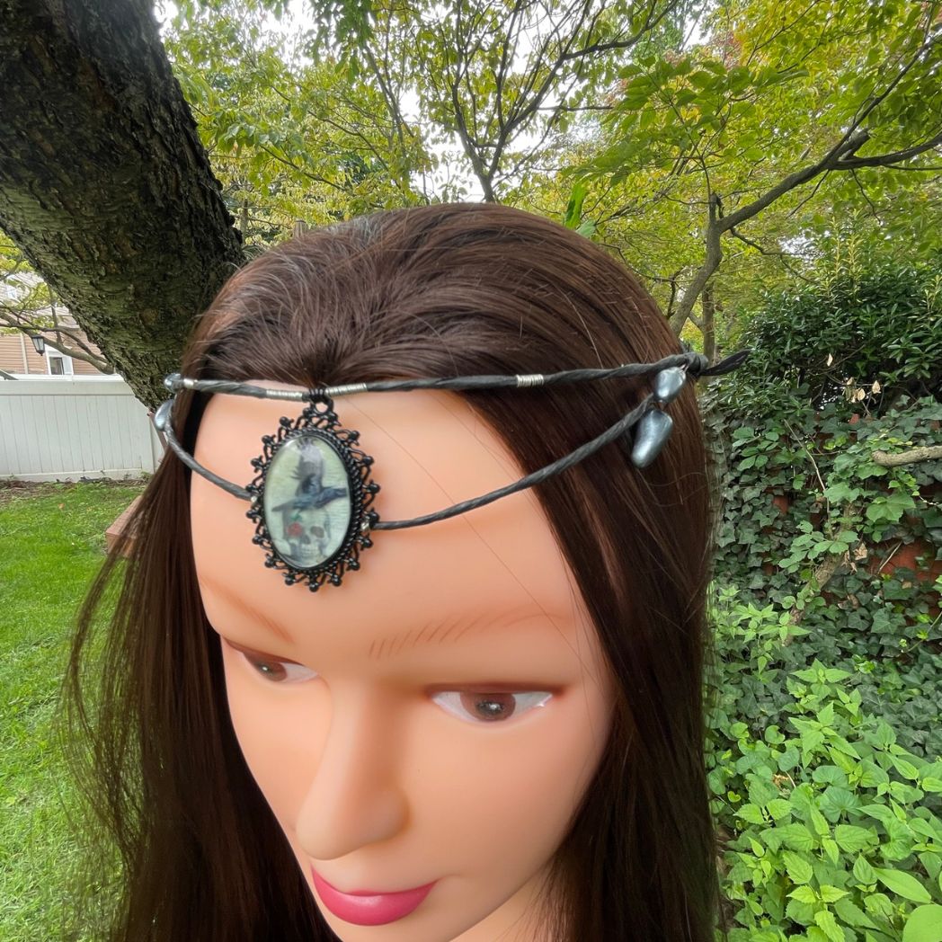 Black wire crown with oval cabochon focal of a raven and skull resting on a model.