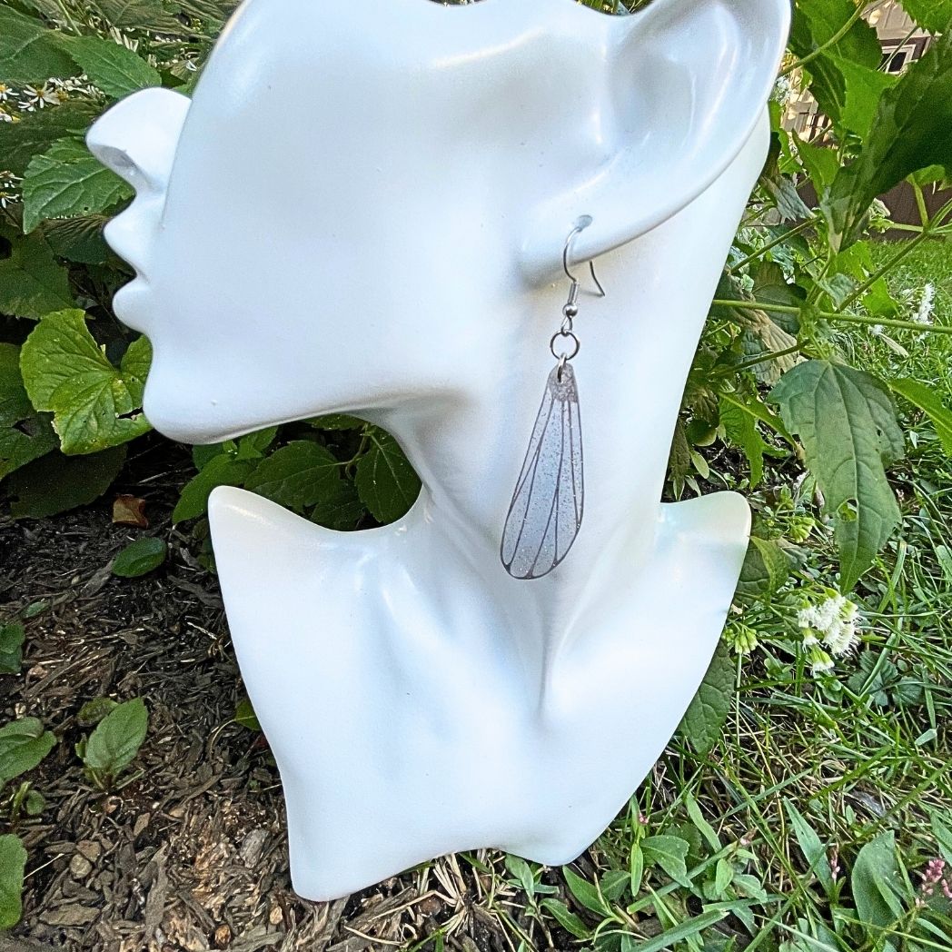Light gray Sparly dragonflly dangle earrings hanging on an earring bust.