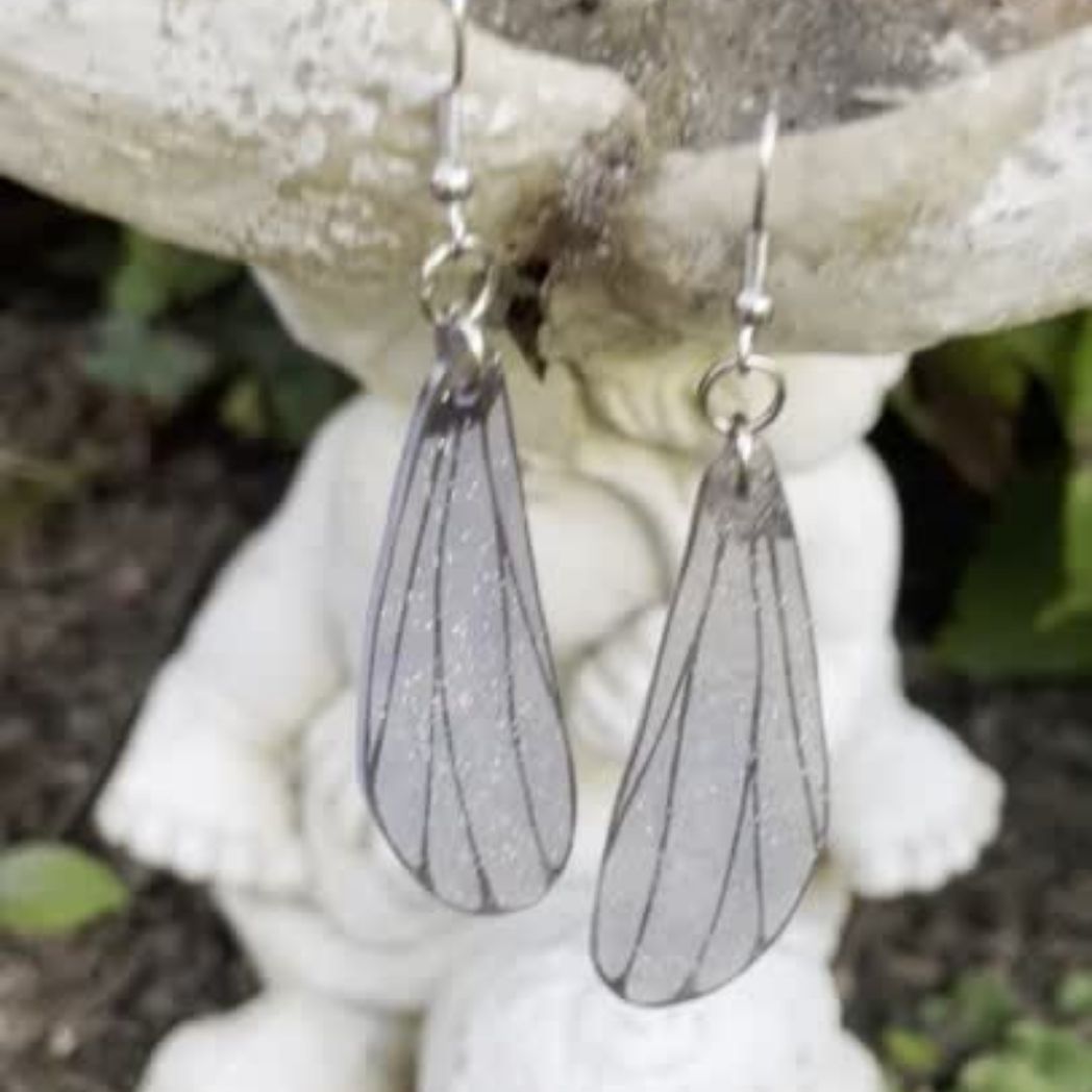 Light gray Sparly dragonflly dangle earrings hanging from a garden ornament.
