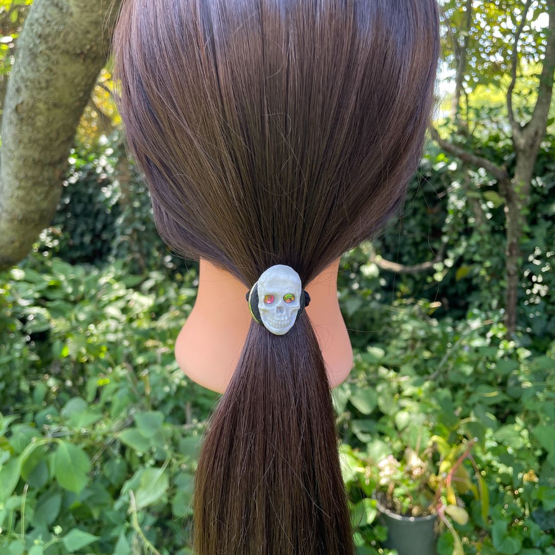 Decorative Hair tie with polymer clay Skull with crystal eyes on a a model set in a garden
