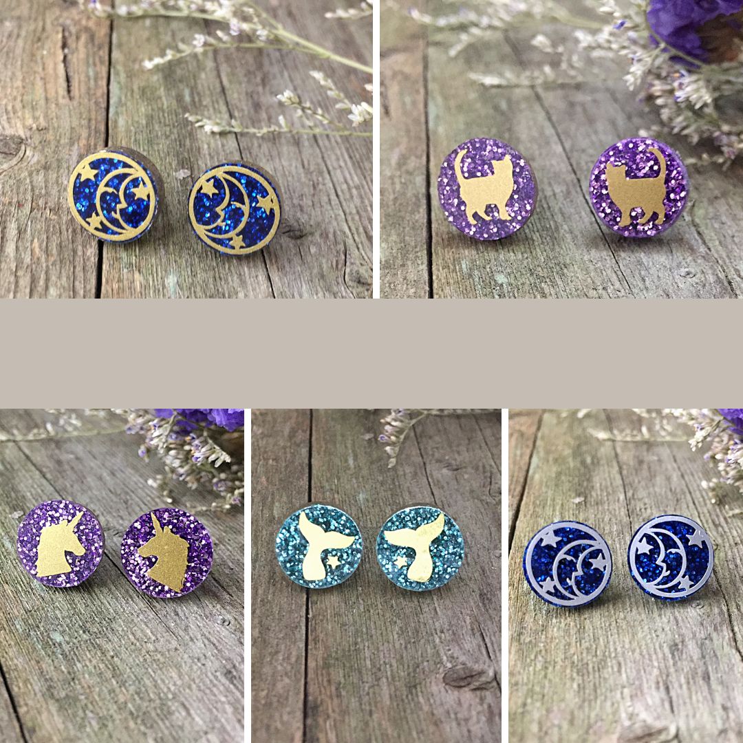 a collection of purple green and blue glitter acrylic earrings with cats, moon, unicorn and fishtail.