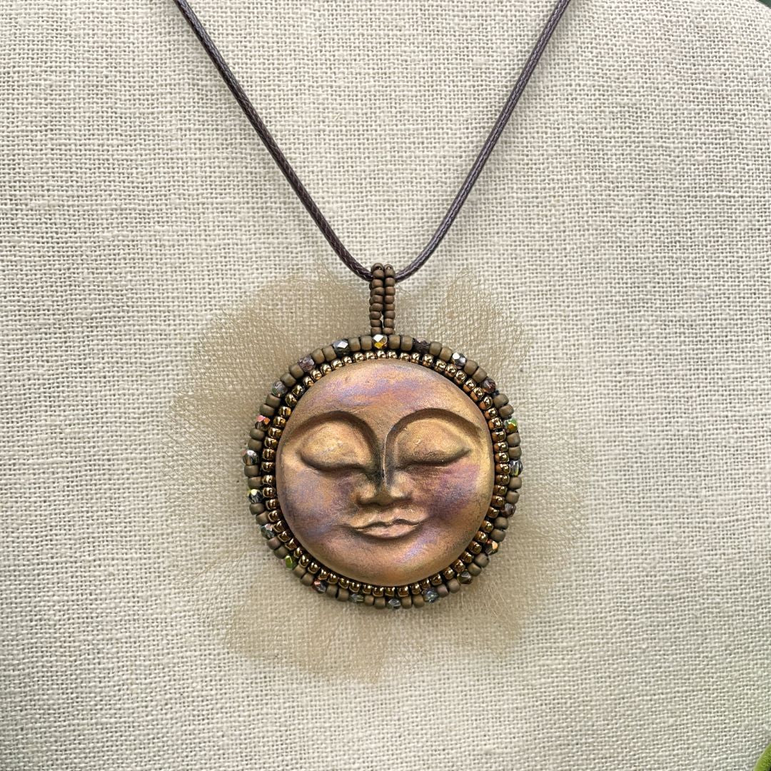 Beaded sun goddess statement pendant with sleeping face and gold beading and tulle around the edge . On a display stand