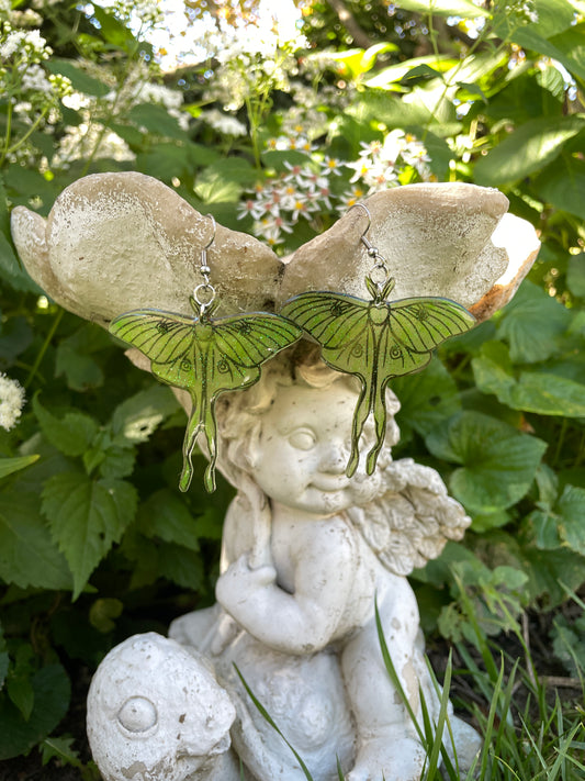 Green luna moth earrings hanging on a garden ornament.