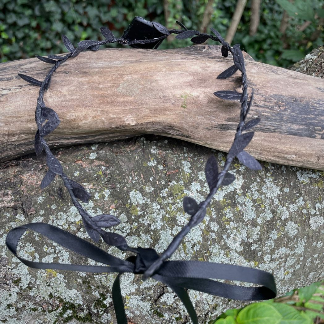 Back of Purple dragon on a diamond shape textured clay base on a black leaf wire headband resting on a tree branch.