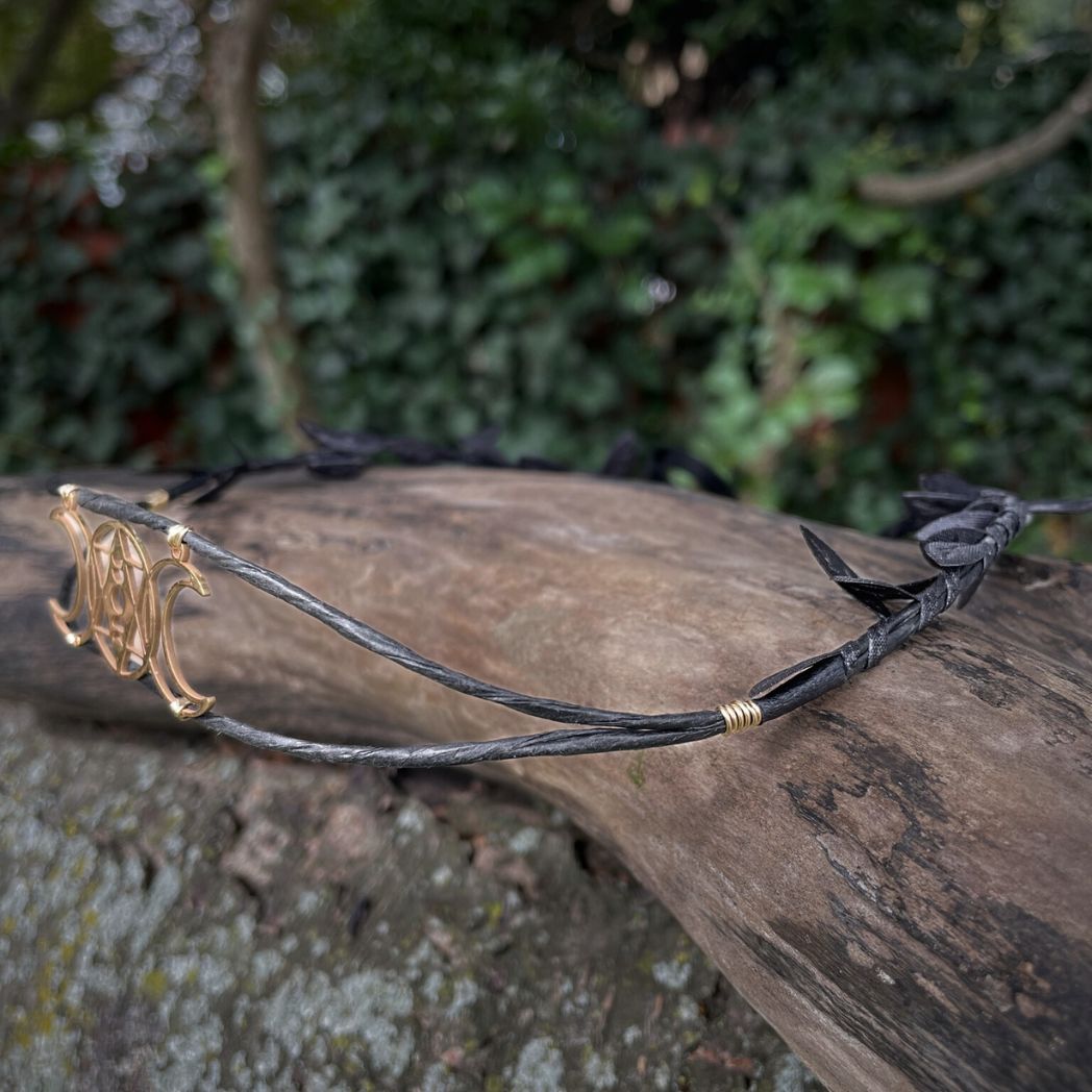 Side profile of triple moon black wired crown sitting on a tree branch
