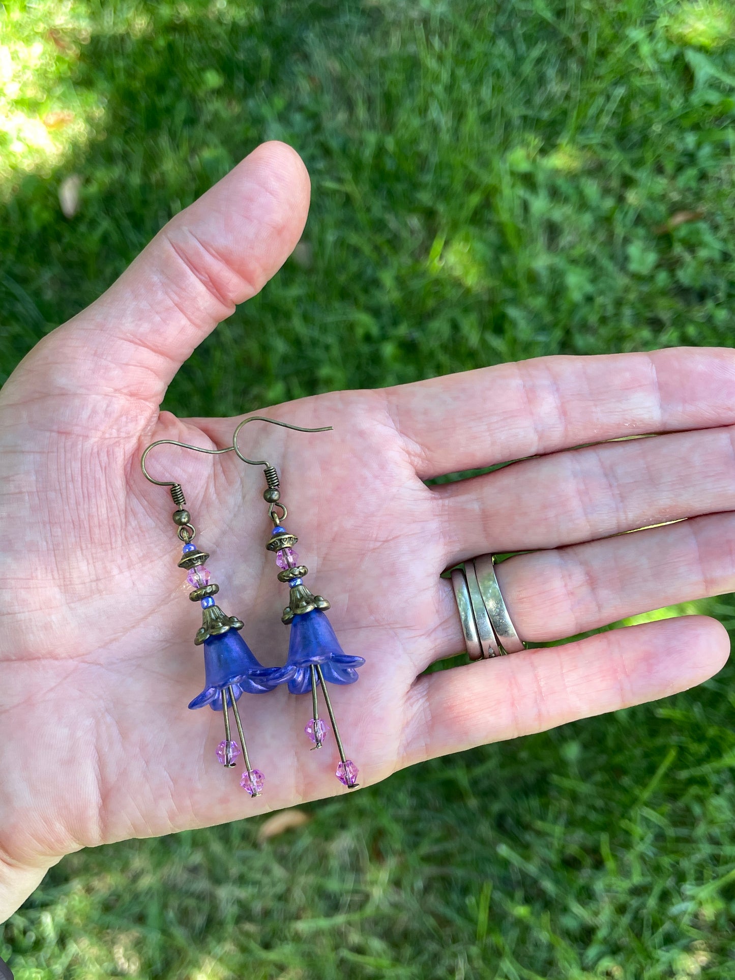 Blue flower dangle earring with antique bronze and purple beads on in a hand  in a garden.