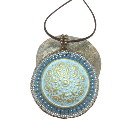 blue floral circle necklace resting on a pebble against a white background.