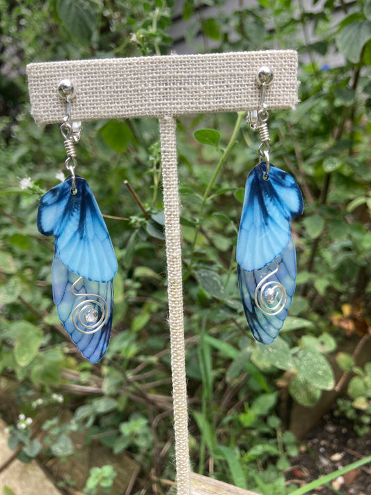 Blue butterfly clip on earring hanging from a display in a garden