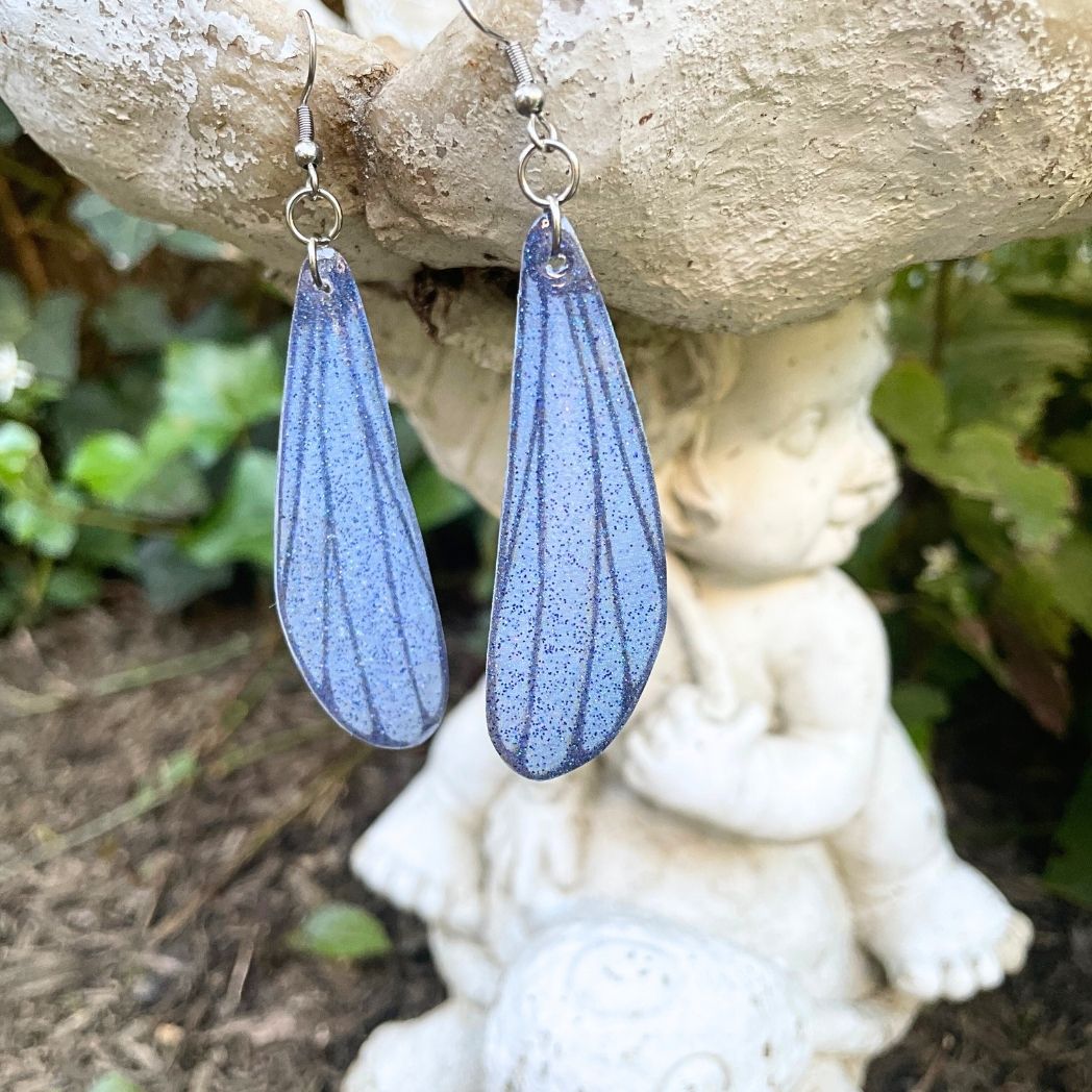 blue gray sparkly dragonfly earrings hanging from a garden ornament.
