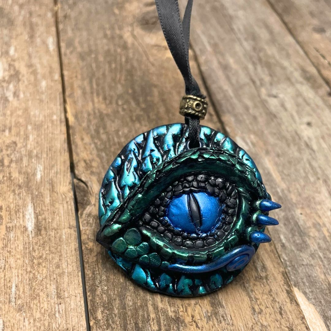 A round dragon eye ornament with metallic green and blue coloring with black satin ribbon .