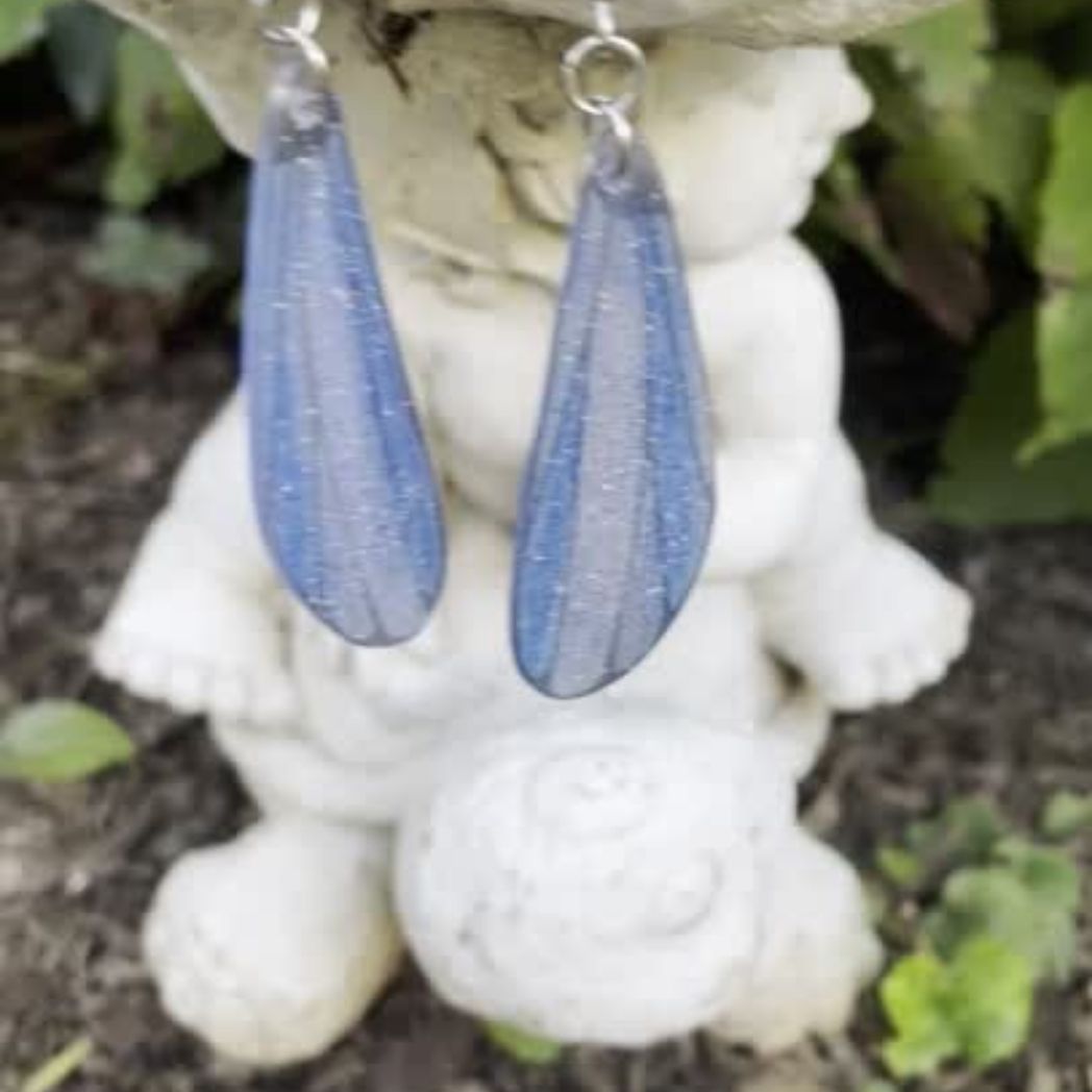 blue and gray sparkly long dangle dragonfly earrings dangling from a garden ornment.