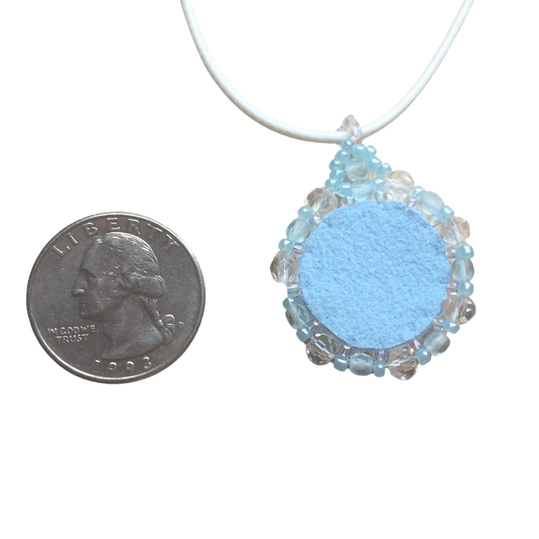 Back of light blue flower necklace against a white background with a quarter  for size reference.