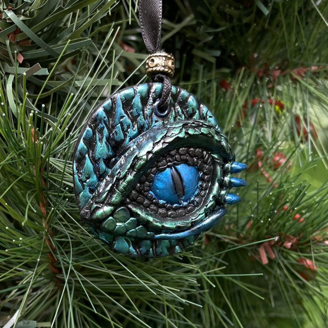 A round dragon eye ornament with metallic green and blue coloring with black satin ribbon hanging on a Christmas tree.