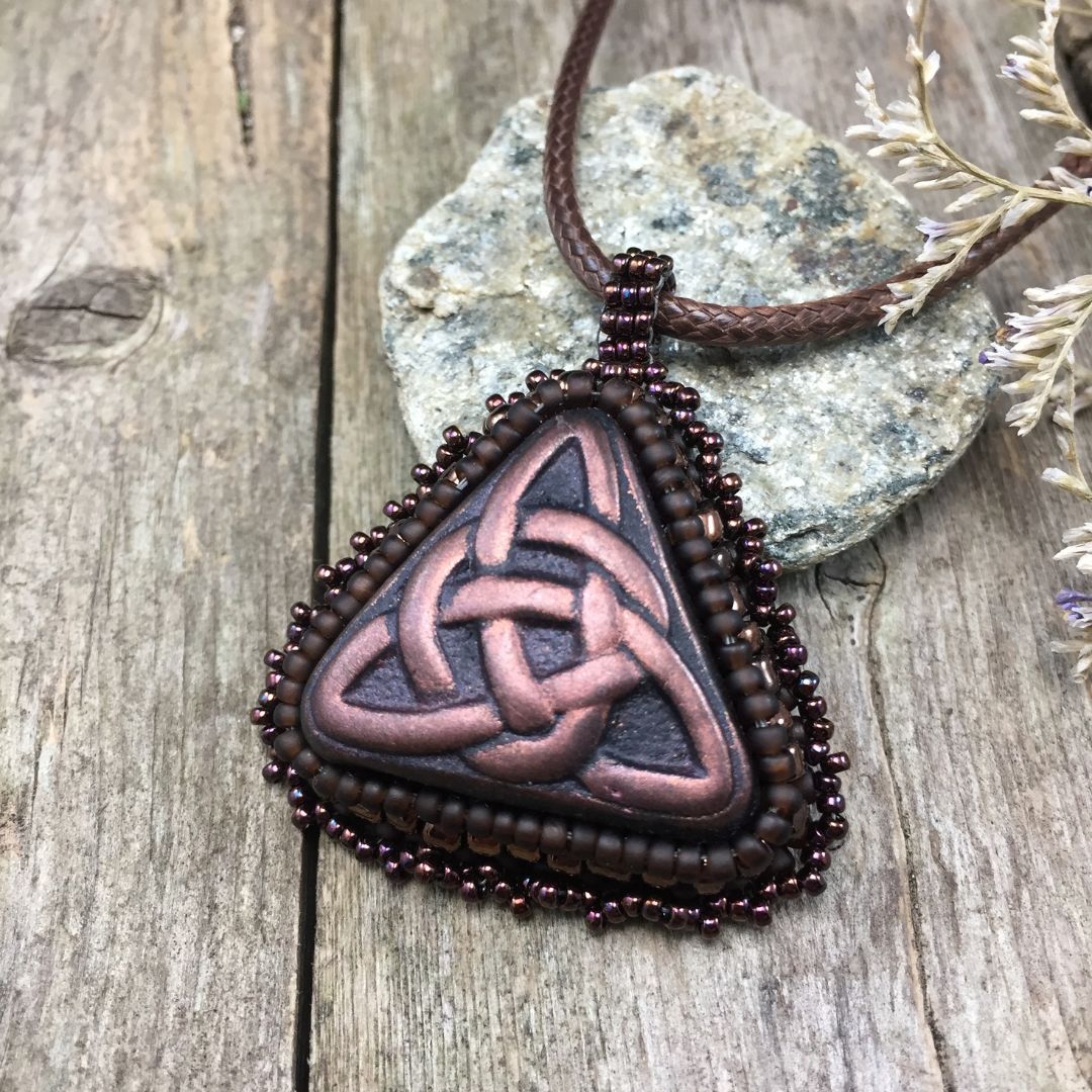 bronze triquetra pendant necklace resting on a pebble on a wood board.