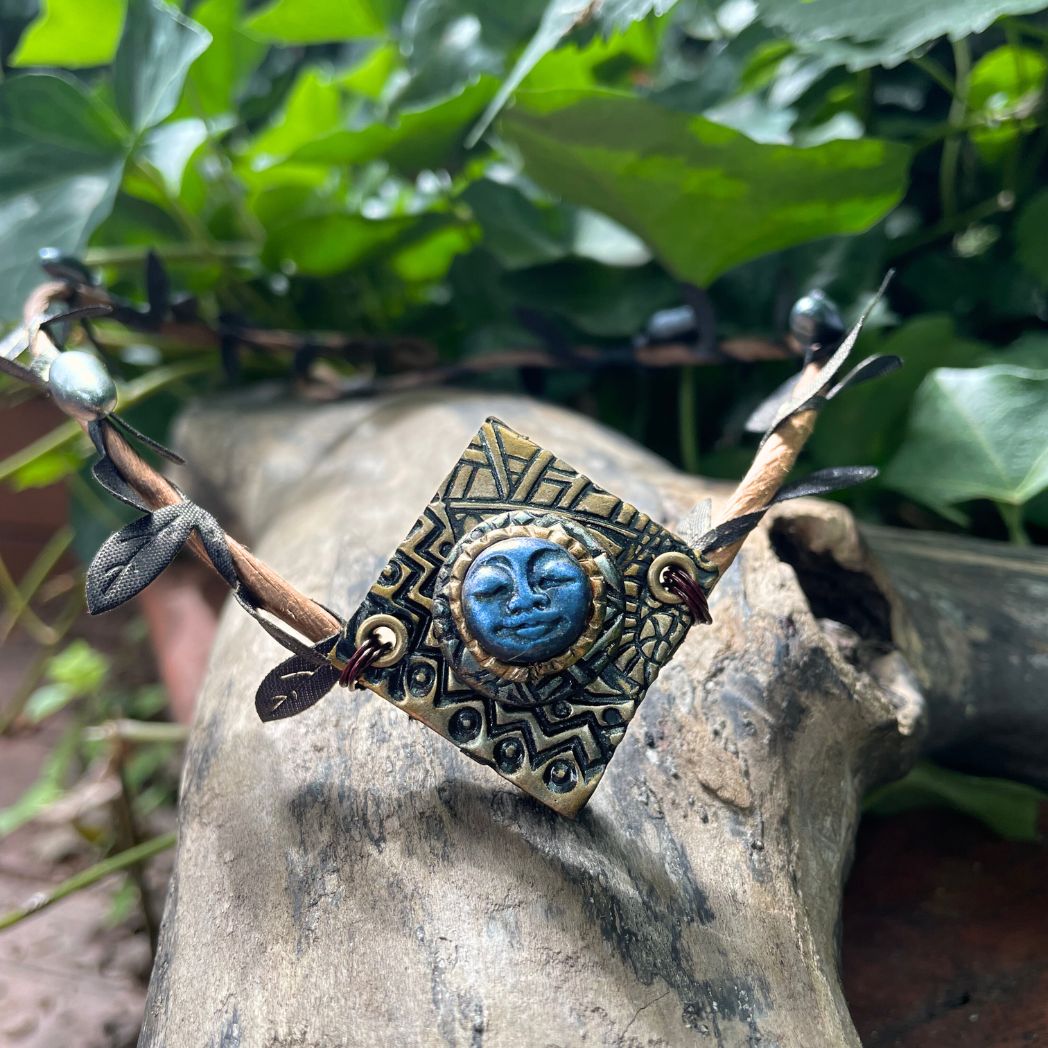 Blue moon on a golden textured diamond shape focal on a brown wire leaf crown resting on a tree branch.