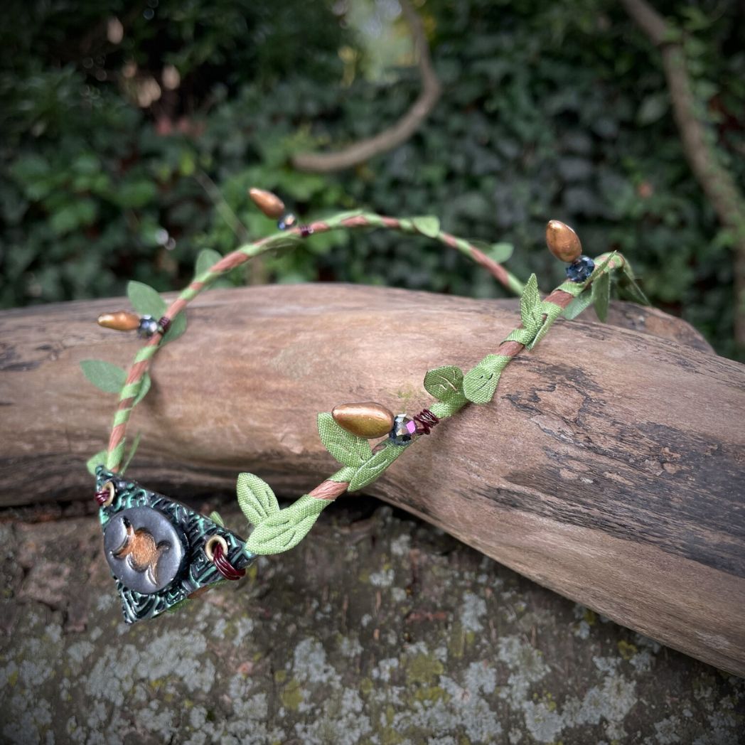 Silver and green triple moon focal on a brown wire and green leaf crown resting on a branch.