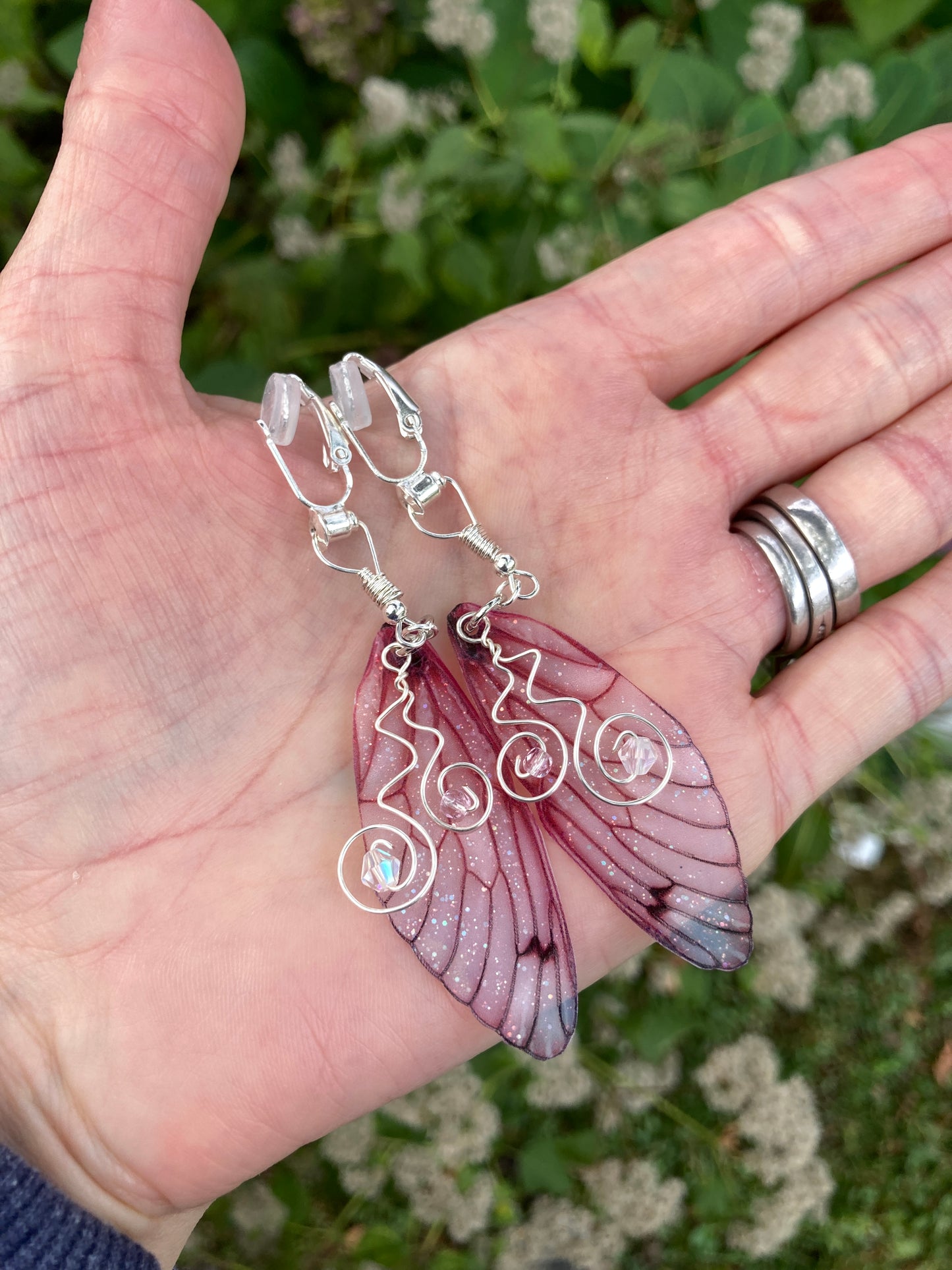 pink butterfly clip on earrings held in a hand outside with greenery