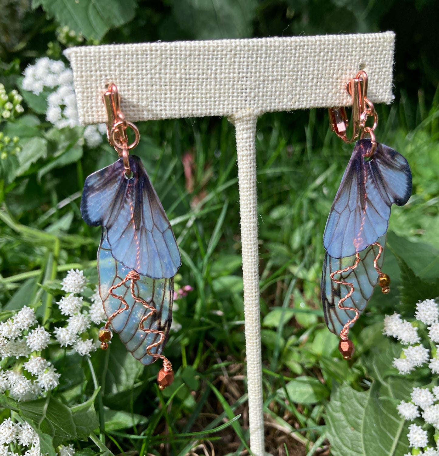 Fairy wing earrings with copper wired crystals with clip on components on an earring stand in  garden