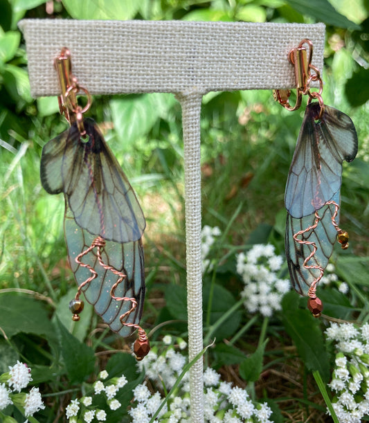 Fairy wing earrings with copper wired crystals with clip on components on an earring stand in  garden