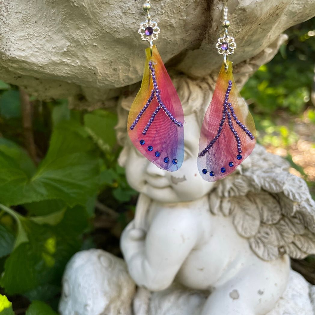 Colorful rainbow sheer fabric with beading and blue crystals. A flower bead with a crystal connects the wings to the ear wires.