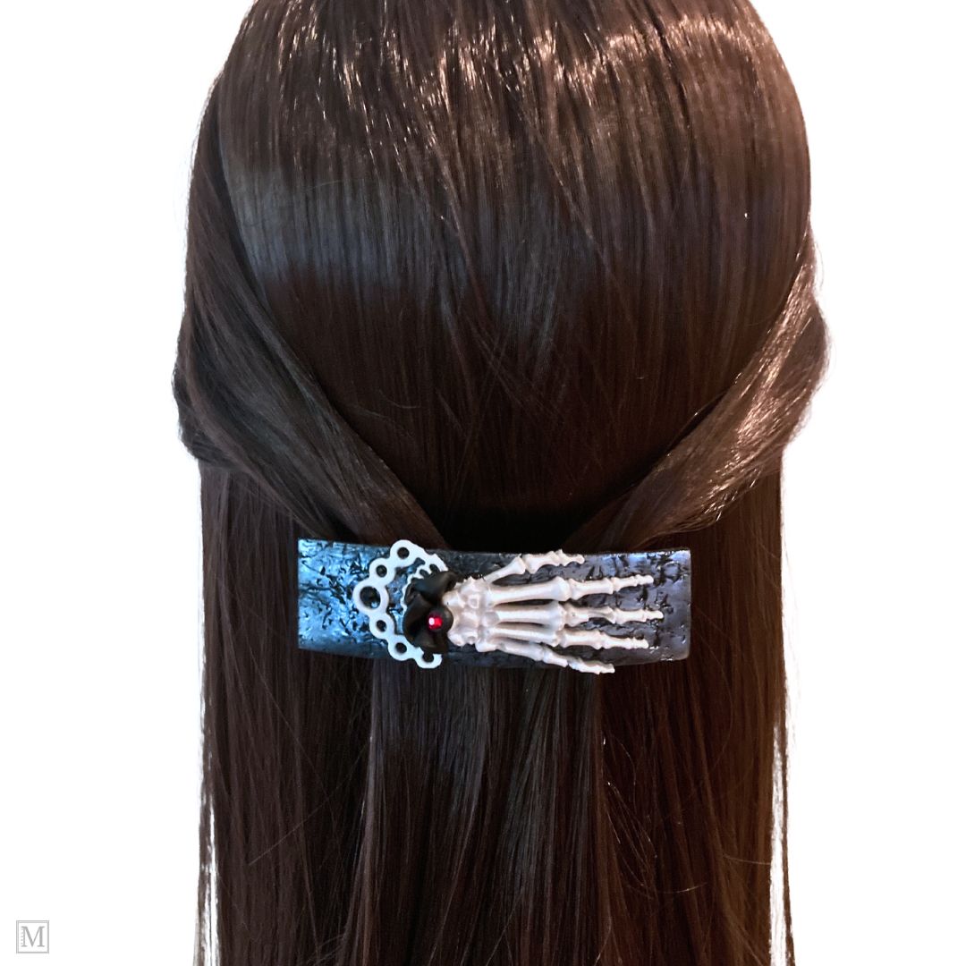 Polymer clay hair barrette with a white skeleton hand on a silver textured clip with a black and white frilly cuff on a model.